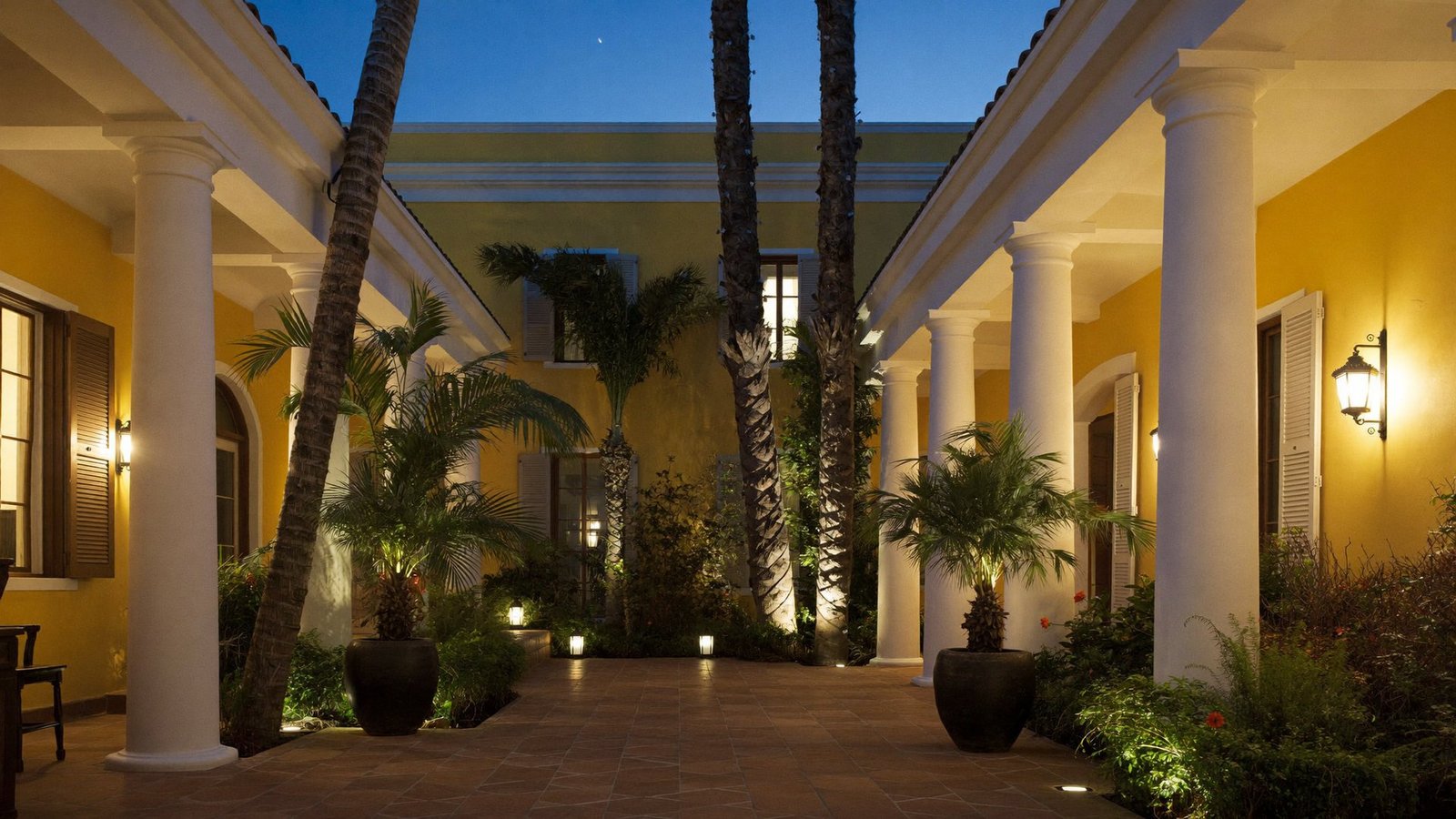 The lamp-lit central courtyard of Gratitude Heritage at blue hour, ringed by white pillars and ochre walls